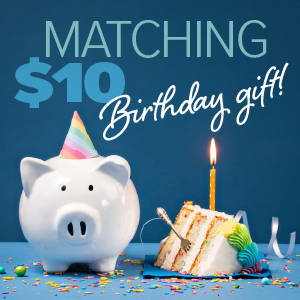 A white piggy bank wearing a colorful birthday hat sits next to a slice of birthday cake