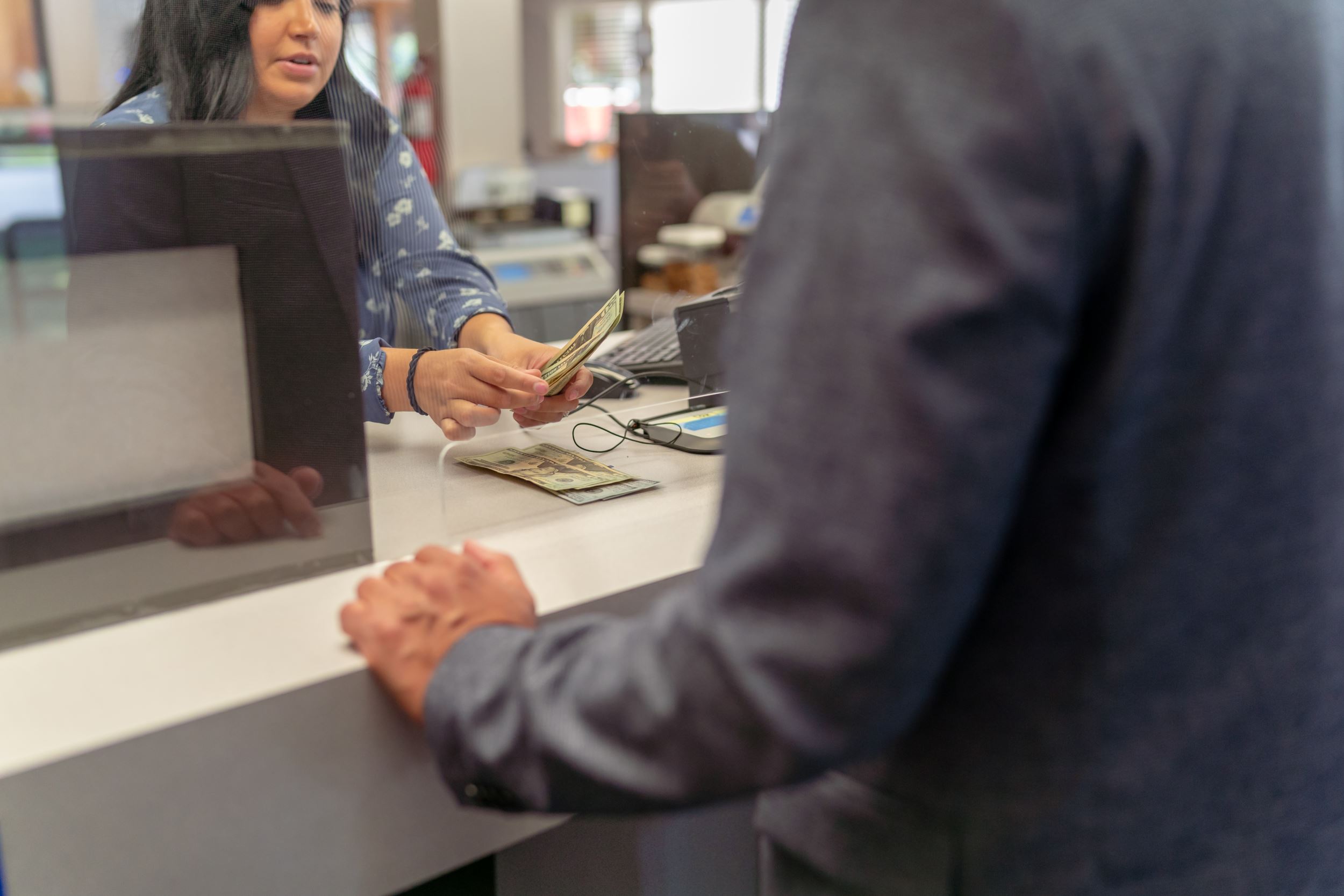 A teller counting cash for a man who's face is not visible in the photo.