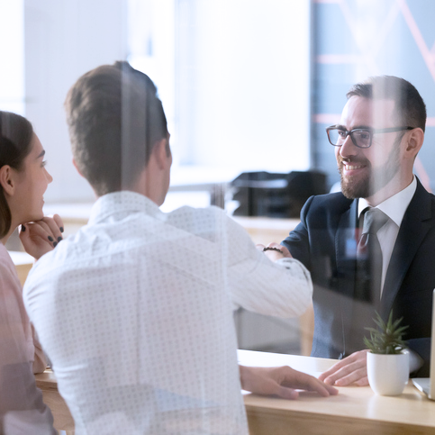 A man shaking hands with a couple at his desk in a brightly lit environment.