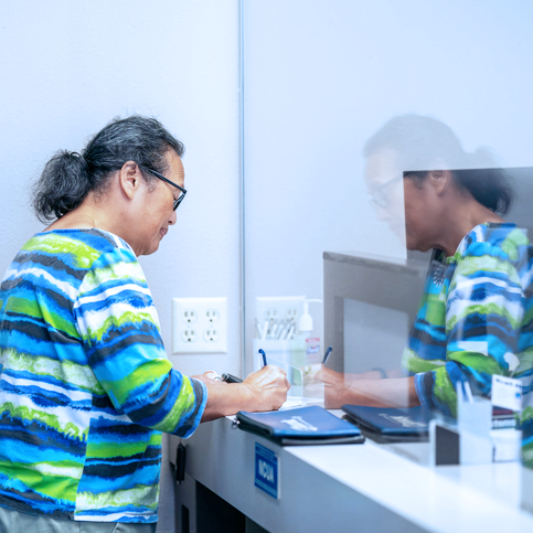 A woman at a bank window writing on a piece of paper.