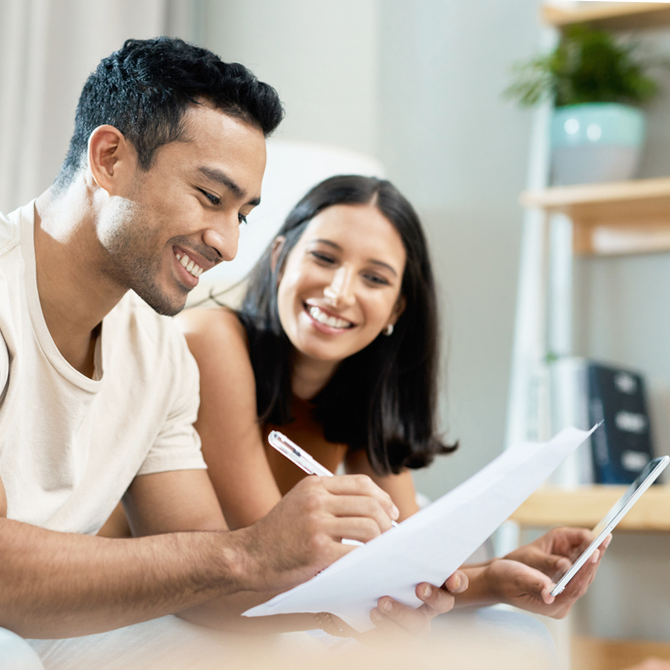A happy interracial couple looking at a document and mobile phone.